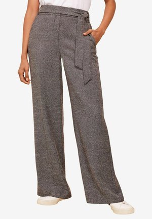 Brede broek in een gestructureerd zwart-wit visgraatpatroon, met een strikriem in de taille en zijzakken, gecombineerd met witte sneakers.