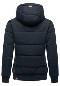 Tamsiai mėlyna pūkinė striukė su užtrauktuku, turinti gobtuvą, vazdus ir juostines rankoves, bei odinę logotipo detalę šonu.