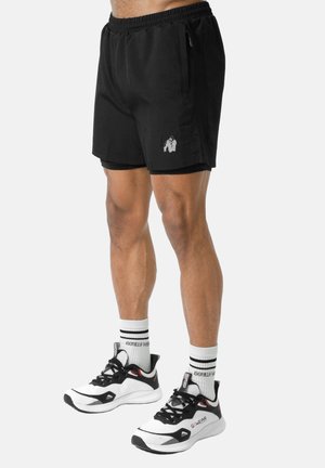 Man draagt zwarte sportshorts met ritssluitingen en witte sportschoenen met bijpassende witte sokken.