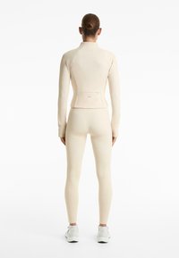 Set atletico beige chiaro composto da una maglietta aderente a maniche lunghe e leggings, con tessuto testurizzato e una tasca sul retro con zip.