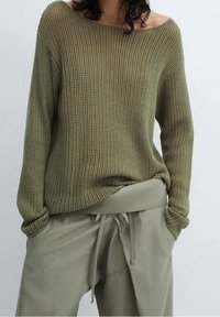 Olijfgroene gebreide trui met een brede halslijn, losse pasvorm en ribbeltextuur, in combinatie met bijpassende taps toelopende joggerbroeken met een trekkoord.