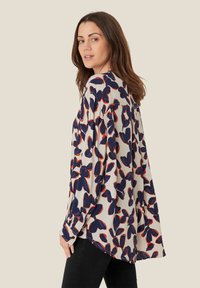 Blusa fluida in tessuto leggero, con uno sfondo crema e grandi motivi floreali in blu navy e rosso. Vestibilità ampia con maniche lunghe.