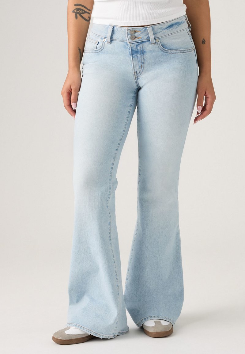 Jeans de ganga azul claro com corte flare, cintura de altura média, cinco bolsos e costuras contrastantes ao longo das costuras.