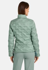 Hellgrüne Puffjacke mit gestepptem Muster, hohem Kragen und schlankem Schnitt, sichtbaren Nähten und elastischen Bündchen.