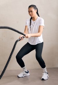 Sportlane, kes kannab valget Nike T-särki ja musti retuuse, kasutab võitlusnööre. Tal on jalas valged ja tumesinised spordijalatsid sobivate spordisokkidega.