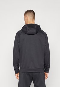 Tamsiai pilka hoody su laisva prigimtimi, su kapišonu, guma apykaklėje ir rankogaliuose, ir lygiu paviršiumi. Nėra matomų logotipų ar raštų.