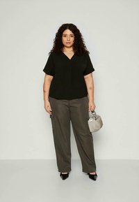Zwarte V-hals blouse met korte mouwen, gecombineerd met losse olijfgroene broek. Accessoires zijn een gestructureerde grijze tas en zwarte hakken.