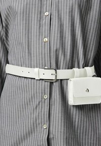 Ceinture en cuir blanc avec une boucle rectangulaire en argent, portée sur une chemise grise à rayures avec des boutons de couleur claire. Comprend une petite pochette blanche.
