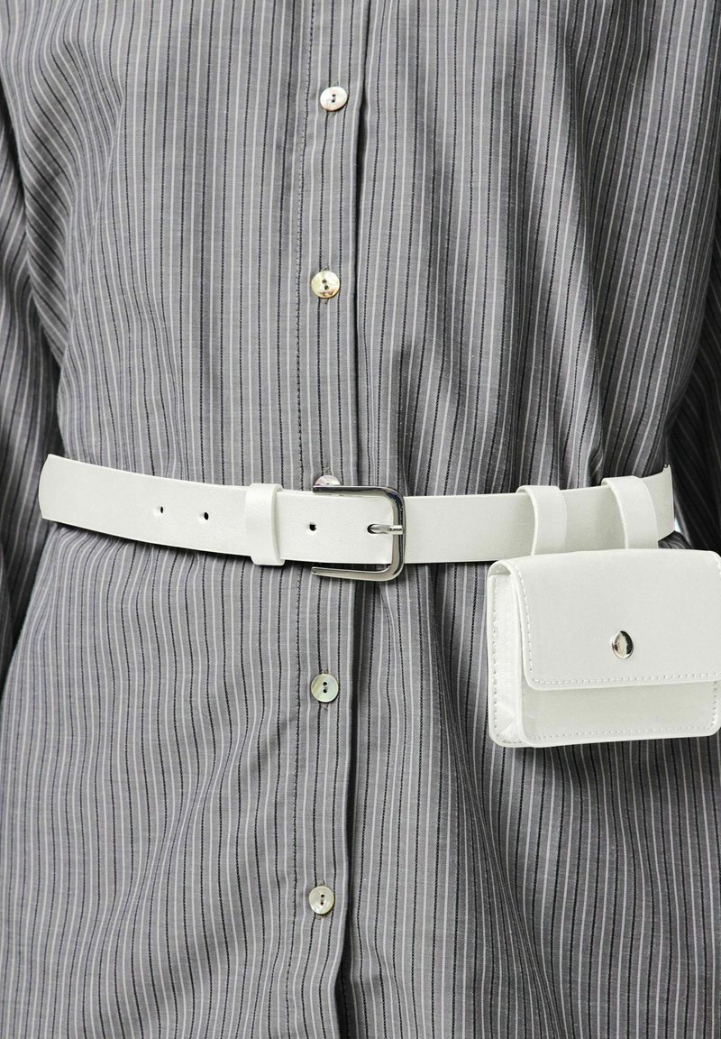 Witte leren riem met een rechthoekige zilveren gesp, gedragen over een grijs gestreept shirt met lichtgekleurde knopen. Inclusief een klein wit tasje.
