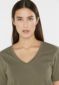 Olive green V-neck t-shirt made of soft cotton fabric. Short sleeves and a relaxed fit, featuring a smooth texture without patterns.