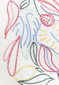 Broderie zigzag colorée formant des formes florales abstraites sur un tissu blanc texturé.