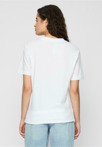 Hvit bomulls t-skjorte, kort erm, rund hals, avslappet passform, jevn tekstur, ingen synlige grafikk eller mønstre, brukt med lyseblå jeans.