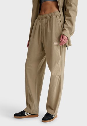 Beige, leichte Hosen mit einem elastischen Bund und Seitentaschen. Kombiniert mit schwarzen Turnschuhen, die beige und weiße Streifen aufweisen.