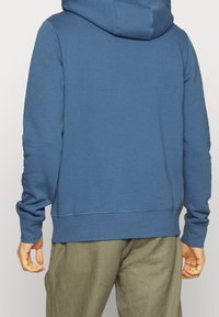 Felpa con cappuccio blu, realizzata in tessuto morbido. Presenta una vestibilità comoda, polsini a coste e un orlo con cuciture a contrasto.