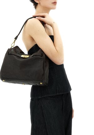 Donna con top nero senza maniche che porta una borsa a tracolla in pelle marrone scuro con chiusura dorata e tracolla.