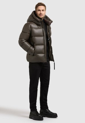 Puffjacka i mörk olivgrön, kviltad design, oversized huva, framzipper, kombinerad med svarta byxor och gedigna svarta kängor.