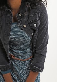 Mörk denimjacka med silverfärgade knappar och en kortad design, lager på lager över en blårandig klänning med flätad bälte.