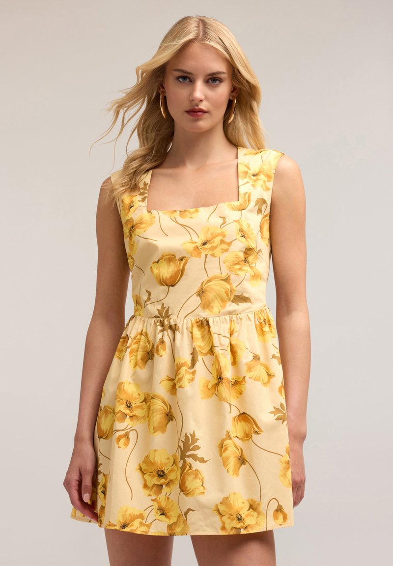 Bloemige katoenen jurk met een vierkante halslijn, voorzien van gele bloemen op een lichtgele achtergrond, met een geplooide taille en mouwloos ontwerp.