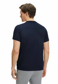 Granatowa koszulka z krótkim rękawem, wykonana z miękkiego materiału, z okrągłym dekoltem i prostym wzorem. Model pokazany od tyłu.