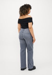 Top preto com ombros à mostra emparelhado com jeans de ganga cinza claro de cintura alta, com bainhas desfiadas e bolsos traseiros, modelo mostrado de costas.