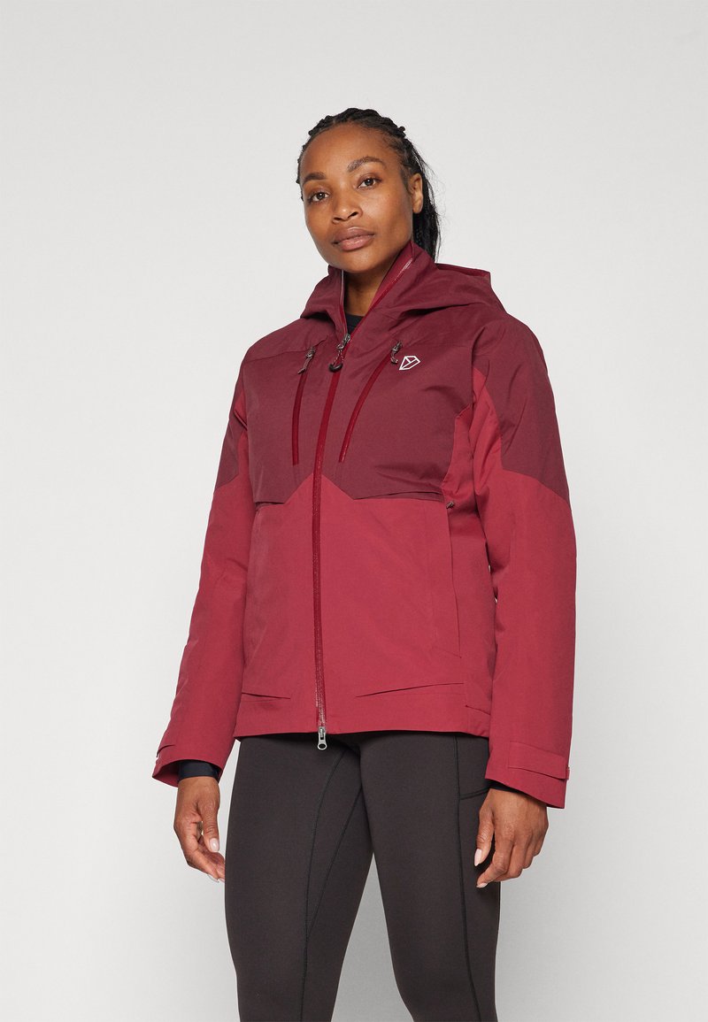 Veste imperméable rouge avec capuche, dotée d'une fermeture éclair sur le devant, de poches latérales et de sections contrastantes rouge foncé sur les épaules et la poitrine.