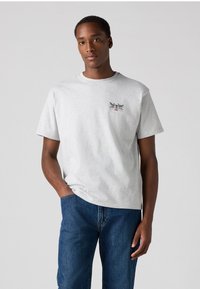 Gray cotton t-shirt with a round neck and short sleeves, featuring a small graphic design on the chest. Worn with blue denim jeans.