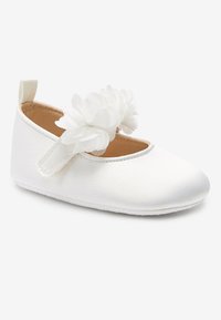 Zapato de bebé de satén blanco con una correa que presenta un grupo de flores de tela blanca, y una lengüeta en el talón.