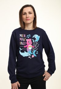 Felpa blu navy con una grafica giocosa che raffigura un orso rosa e dei delfini, con elementi colorati e la scritta "MERMAZING!" in lettere in grassetto.
