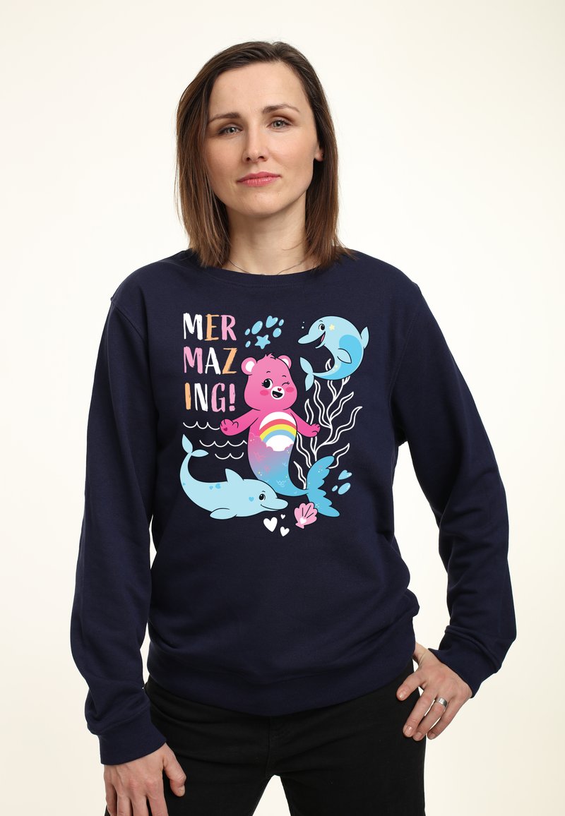Felpa blu navy con una grafica giocosa che raffigura un orso rosa e dei delfini, con elementi colorati e la scritta "MERMAZING!" in lettere in grassetto.