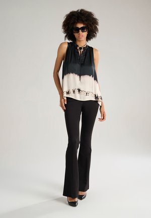 Black and cream sleeveless top with a silky texture, featuring a button placket, dip-dye design, and a flowing silhouette, paired with black flared pants.