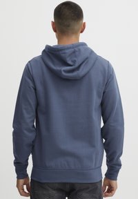 Felpa blu con tasca a marsupio, cappuccio regolabile con coulisse, polsini e orlo in costina. Il tessuto sembra morbido e liscio con una vestibilità comoda.