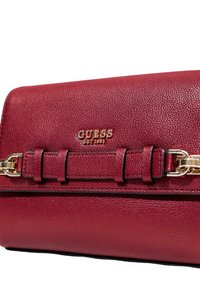 Borsa in pelle rossa con hardware dorato, caratterizzata da una superficie testurizzata, una tracolla decorativa e il logo in rilievo "GUESS EST 1981".