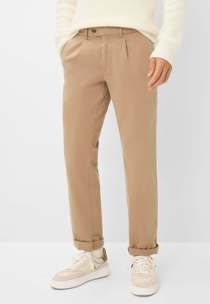 Beige Baumwollhosen mit lockerer Passform, ausgestattet mit Vorderfalten und aufgerollten Bündchen, kombiniert mit weißen und beigen Sneakers.
