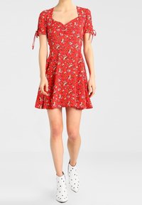 Rotes Blumenkleid mit kurzen Ärmeln, Herzausschnitt und Schleifen-Details an den Ärmeln, kombiniert mit weißen Knöchelstiefeln, die mit Nieten verziert sind.