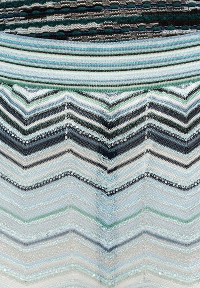 Detail pletenej textílie s horizontálnymi pruhmi a vzormi v tvare rybej kosti v odtieňoch modrej, zelenej, čiernej a bielej.