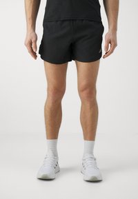 Svarta idrottsshorts i lättviktsmaterial, med en avslappnad passform och diskret varumärkeslogotyp. Parat med vita sneakers och strumpor.