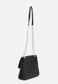 Czarna torebka wykonana z gładkiego materiału, z pikowanym przodem, złotym łańcuszkiem oraz sztywną formą z zapięciem na klapkę.