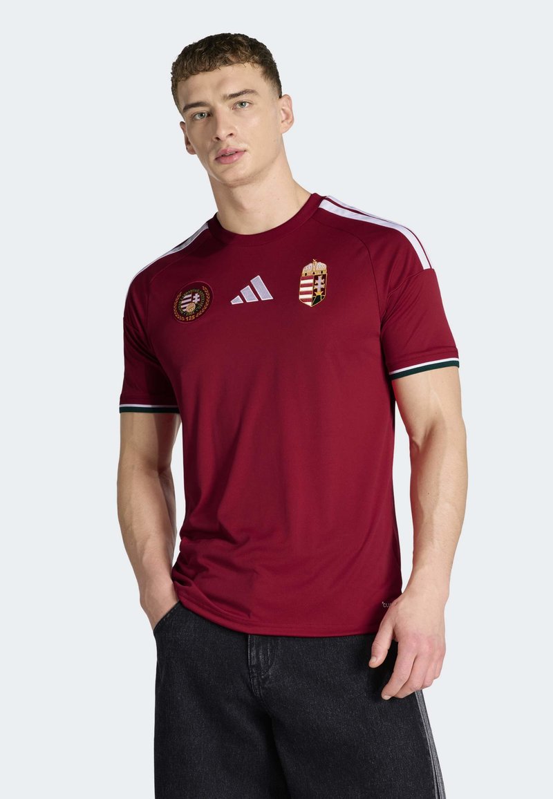 Vinrød atletisk trøje med hvide striber på skuldrene, med broderet Ungarns våbenskjold og rundt embleme. Fremstillet af letvægtsstof.