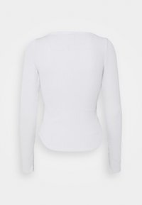 Top bianco a maniche lunghe con design aderente, scollatura rotonda e orlo leggermente curvato. Il tessuto testurizzato aumenta l'interesse visivo.