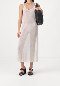 Vestido maxi de malla blanca translúcida con escote en V, tirantes finos ajustables y corte holgado. Combinado con sandalias de tacón bloque negras con hebillas doradas.