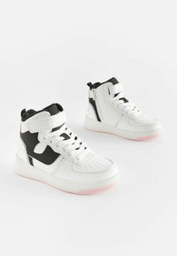 Sneakers înalte din piele albă, cu accente negre și tălpi de cauciuc roz. Au șireturi și un fermoar lateral pentru închidere. Design perforat la vârf.