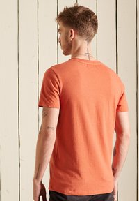 Orange kortærmet t-shirt med rund halsudskæring. Har en blød tekstur og lige snit, præsenteret mod en lys træbaggrund.