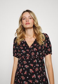 Vestido floral preto com mangas curtas, apresentando um decote em V e um pequeno padrão de flores multicoloridas. Tecido suave e um design ajustado.