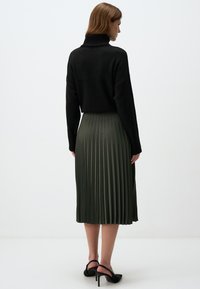 Schwarzer Rollkragenpullover kombiniert mit einem plissierten, knielangen olivgrünen Rock. Besitzt glatte Texturen und eine taillierte Silhouette.