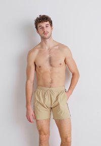 Shorts de bain beiges en matériau léger, dotés d'une ceinture élastique avec cordon de serrage et de rayures sur les côtés.