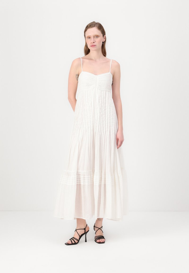 Rochie maxi albă, fără mânici, cu dungi verticale texturate, un corset ajustat și o fustă vaporoasă, asortată cu sandale negre cu siret.
