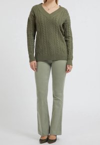 Maglione verde oliva a treccia con scollatura a V, abbinato a pantaloni a palazzo verde oliva chiaro e scarpe a punta dello stesso colore.