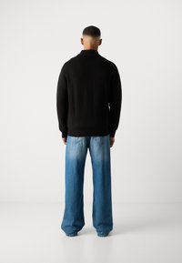 Pull en maille noir à col haut, associé à un jean large bleu clair avec un dégradé usé et des poches arrières.