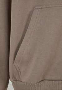 Tela de sudadera marrón con un bolsillo tipo canguro, dobladillo ribeteado y puños; textura suave con un ligero estiramiento.