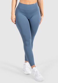 Leggings blu a vita alta realizzati in un tessuto elasticizzato, con una texture liscia e un design senza cuciture. Abbinati a scarpe da ginnastica bianche.